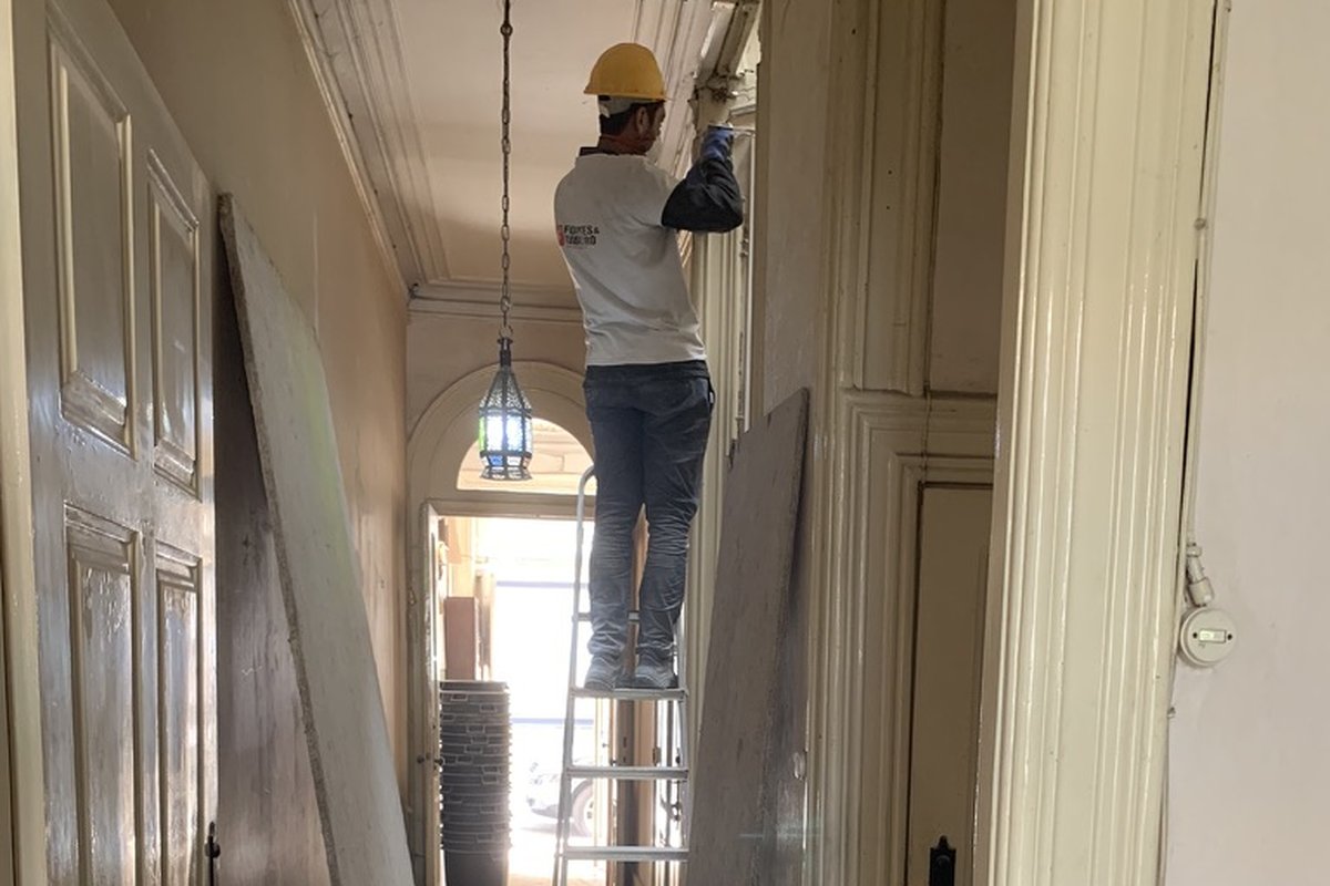 Ouvrier sur un escabeau lors de la rénovation d'un appartement ancien à Porto, portes démontées et murs décapés